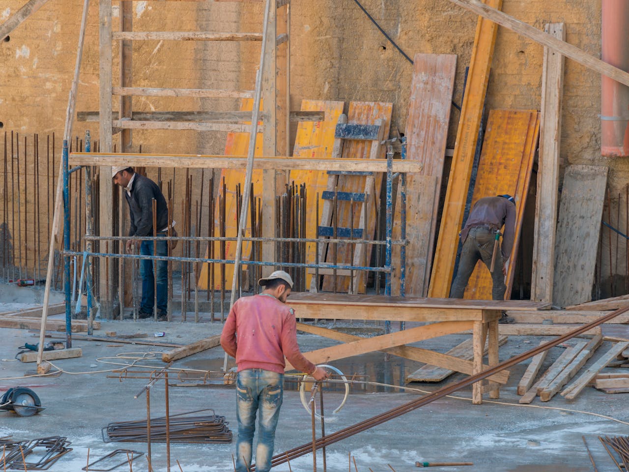 Three construction workers assembling wooden scaffolding on an outdoor construction site.