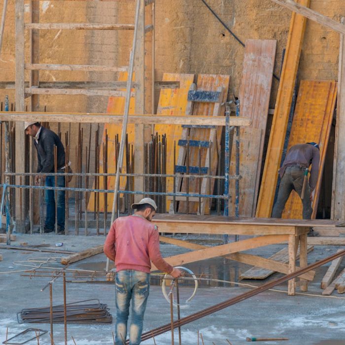 Three construction workers assembling wooden scaffolding on an outdoor construction site.